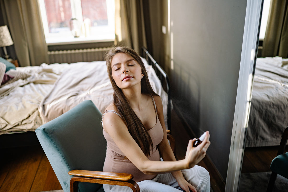 Woman with eyes closed spraying fragrance in a sunlit bedroom