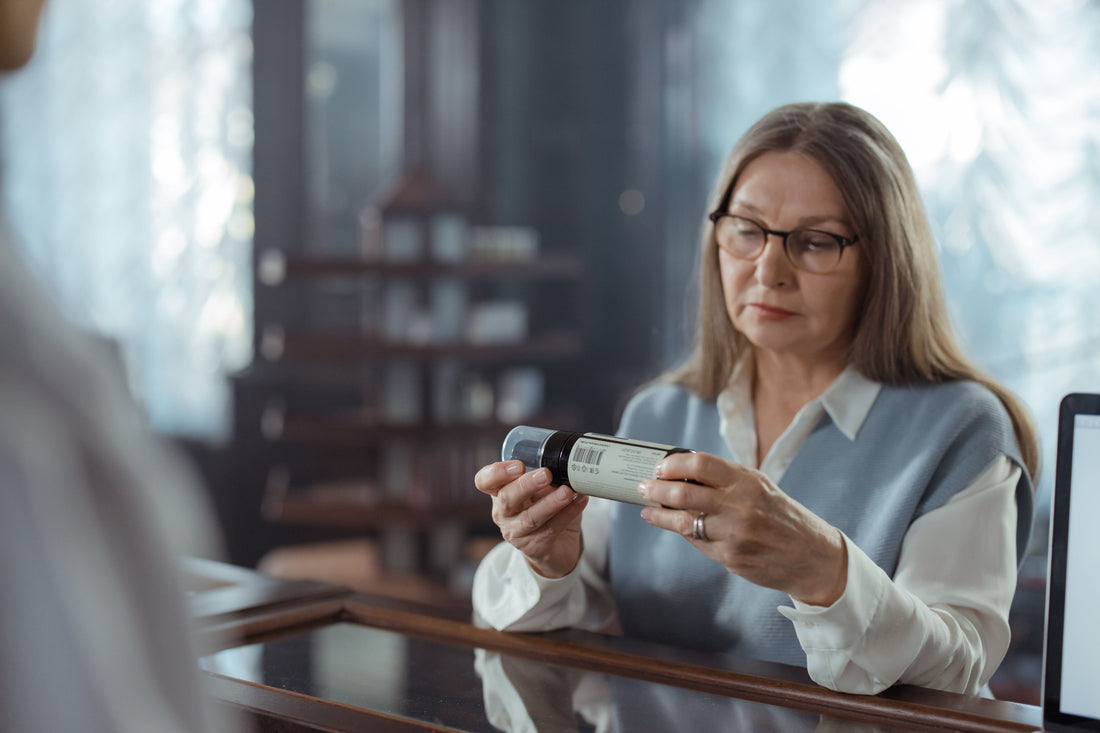 Woman thoughtfully reading a product label on a bottle indoors